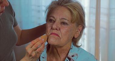 Age makeup. Applying cream with a sponge to an 85-year-old woman with blue eyes video