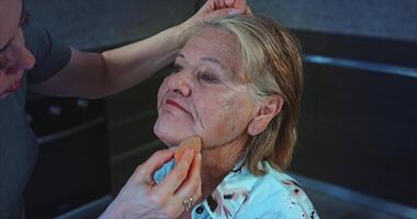 Age makeup. Applying foundation with a sponge to an 85-year-old woman with blue eyes video