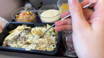 de cerca de un mujer come pasta con carne desde un el plastico envase en el avión. mujer comiendo comida en comercial avión. personas comer en el avión. pasajeros disfrutar un caliente almuerzo durante el vuelo. video