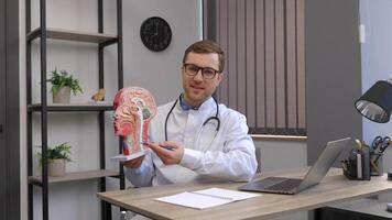 A young attractive otolaryngologist doctor shows a model of the human head and tells the patient about the structure of the respiratory system video