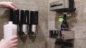 Woman fills shampoo dispenser in shower stall. Bathroom and marble tile. video
