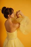 Profile portrait of a beautiful middle-aged woman in a yellow dress, her hair pulled up against a yellow background photo