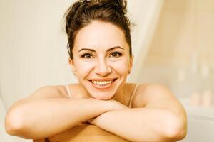 Portrait of a middle-aged woman, smiling with her arms folded in front of her face, her hair pulled up. The brunette is in a good mood. On a light background. photo