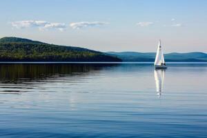 Sailboat drifting lazily on calm lake, its sails billowing in the gentle summer breeze photo