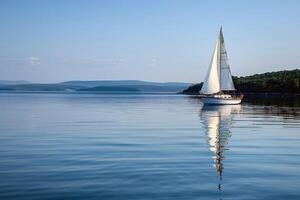 Sailboat drifting lazily on calm lake, its sails billowing in the gentle summer breeze photo