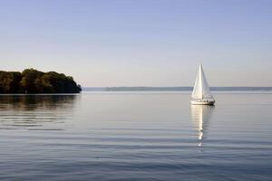 Sailboat drifting lazily on calm lake, its sails billowing in the gentle summer breeze photo