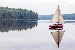 Sailboat drifting lazily on calm lake, its sails billowing in the gentle summer breeze photo