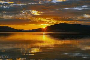 Sunset over tranquil lake, casting warm glow over the water and surrounding landscape photo