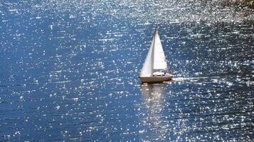 Sailboat gliding across sparkling blue waters, propelled by gentle summer breeze photo