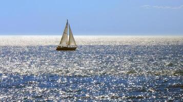 Sailboat gliding across sparkling blue waters, propelled by gentle summer breeze photo