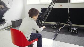 Boy sits in the excavator simulator and plays with the joystick. Transportation of steel cubes using a magnet. video