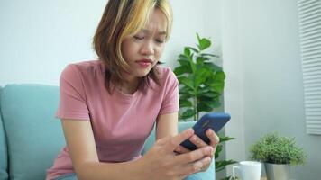 femme est séance sur une canapé et à la recherche à sa cellule téléphone. elle est dérangé ou frustré video