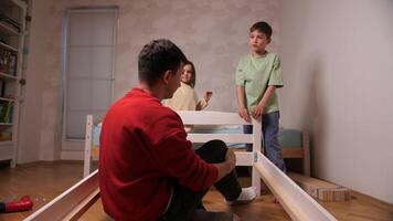 dad high-fives his kids.Children help dad assemble the bed. Boy and little girl video