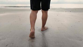 4k imagens de vídeo, pés do homem comovente lentamente andar descalço em a de praia dentro manhã. masculino turista durante verão período de férias dentro chao lao praia, chanthaburi, Tailândia video