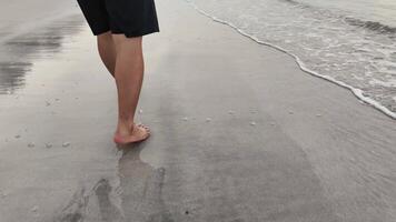 4k imagens de vídeo, pés do homem comovente lentamente andar descalço em a de praia dentro manhã. masculino turista durante verão período de férias dentro chao lao praia, chanthaburi, Tailândia video