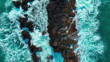 aérien Haut vue de vagues Pause sur rochers dans une bleu océan. mer vagues sur magnifique plage aérien vue drone. des oiseaux œil vue de océan vagues s'écraser contre un vide pierre Roche falaise de au dessus video