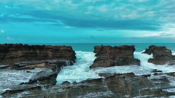 aerial top view of waves break on rocks in a blue ocean. sea waves on beautiful beach aerial view drone. bird's eye view of ocean waves crashing against an empty stone rock cliff from above video