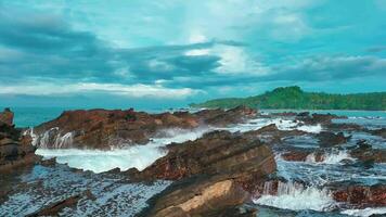 aerial top view of waves break on rocks in a blue ocean. sea waves on beautiful beach aerial view drone. bird's eye view of ocean waves crashing against an empty stone rock cliff from above video