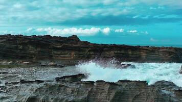 aérien Haut vue de vagues Pause sur rochers dans une bleu océan. mer vagues sur magnifique plage aérien vue drone. des oiseaux œil vue de océan vagues s'écraser contre un vide pierre Roche falaise de au dessus video