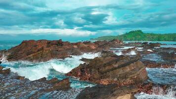 aerial top view of waves break on rocks in a blue ocean. sea waves on beautiful beach aerial view drone. bird's eye view of ocean waves crashing against an empty stone rock cliff from above video