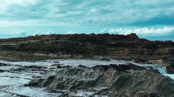 aérien Haut vue de vagues Pause sur rochers dans une bleu océan. mer vagues sur magnifique plage aérien vue drone. des oiseaux œil vue de océan vagues s'écraser contre un vide pierre Roche falaise de au dessus video
