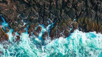 aéreo topo Visão do ondas pausa em pedras dentro uma azul oceano. mar ondas em lindo de praia aéreo Visão drone. pássaro olho Visão do oceano ondas falhando contra a esvaziar pedra Rocha penhasco a partir de acima video