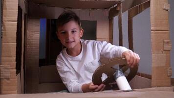 fermer de une garçon séance dans une papier carton voiture et tournant le pilotage roue video