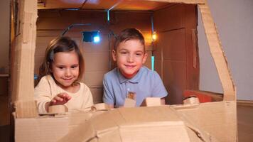 Boy and girl playing with a cardboard spaceship. Children play astronauts video