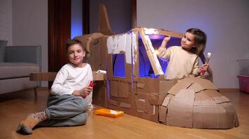 Brother and sister play together at home. kids built airplane out of cardboard video