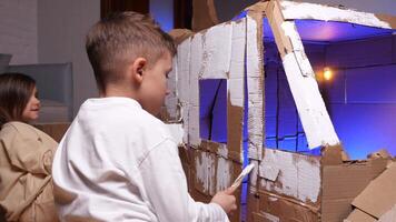 A boy and girl paints the cabin of a cardboard spaceship with a brush. video