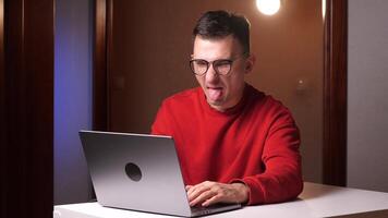 a young man works at a laptop and shows his tongue. Internet commentator concept video