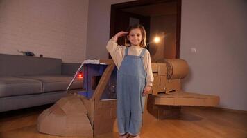 weinig meisje maakt een leger groet, groet De volgende naar ruimteschip gemaakt van karton video