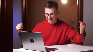 joven chico en un lentes leyendo bueno Noticias en su computadora a trabajar. ganar gesto video