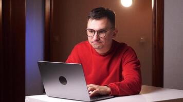 enojado insatisfecho hombre con lentes mecanografía un mensaje en un ordenador portátil video