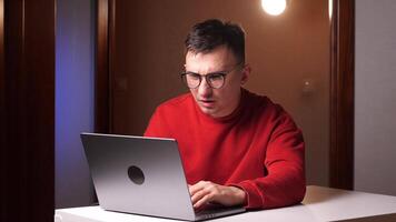 a man in a red sweatshirt reads bad news on a laptop, makes a mistake at work video