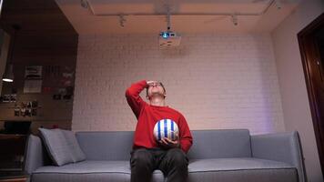 futebol ventilador dentro vermelho às casa é intensamente assistindo a jogo, agarrando dele cabeça video