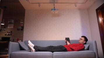 man lying on sofa searching for online film or TV series to watch for fun. video