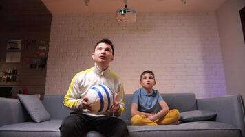 father and son watching a football match at home together video