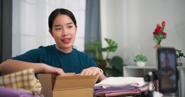 antal fot dolly skott, ung asiatisk kvinna företag ägare försäljning kläder leva strömning på mobil telefon och packade kläder in i låda för en kund ,uppkopplad handla video