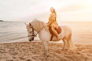 un mujer en un vestir soportes siguiente a un blanco caballo en un playa, con el azul cielo y mar en el antecedentes. foto