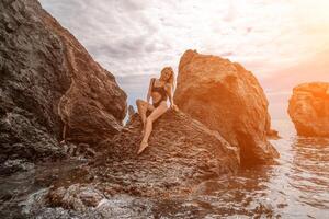 mujer viaje mar. atractivo rubia mujer en un negro traje de baño disfrutando el mar aire en el costa alrededor el rocas viaje y vacaciones concepto. foto