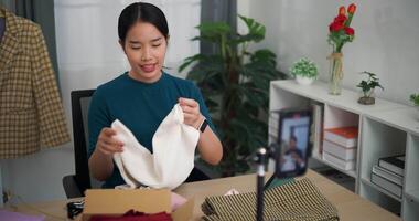 antal fot hög vinkel se skott, ung asiatisk kvinna företag ägare försäljning kläder leva strömning på mobil telefon visa ny samling mode kläder till kund ,uppkopplad handla video