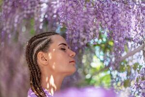 Woman wisteria lilac dress. Thoughtful happy mature woman in purple dress surrounded by chinese wisteria photo