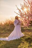 Woman blooming peach orchard. Against the backdrop of a picturesque peach orchard, a woman in a long white dress enjoys a peaceful walk in the park, surrounded by the beauty of nature. photo