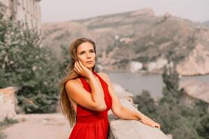 Woman red dress. Summer lifestyle of a happy woman posing near a fence with balusters over the sea. photo