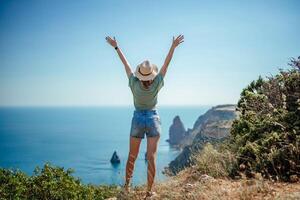 Woman tourist sky sea. Happy traveller woman in hat enjoys vacation raised her hands up photo