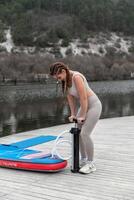 un mujer es en pie en un muelle con un tabla de surf y un bomba. ella es vistiendo un bikini y tiene rastas. foto