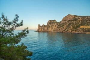 A beautiful blue ocean with a rocky shoreline. The sky is clear and the sun is setting. photo