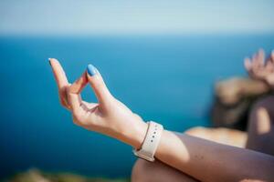 A woman is sitting on a rock by the ocean, with her hand in a prayer position photo