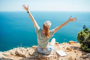 Woman tourist sky sea. Happy traveller woman in hat enjoys vacation raised her hands up photo
